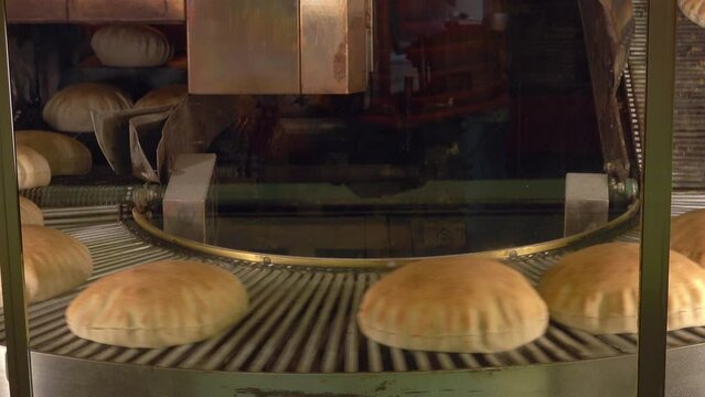 Real time of freshly baked round shaped bread placed on conveyor belt at industrial factory