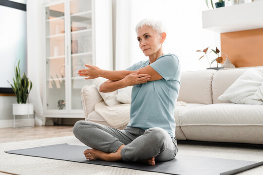 Sporty Caucasian woman in fitness clothes doing training at home on sporty mat. Female athlete stretching arms in lotus yoga position on the floor