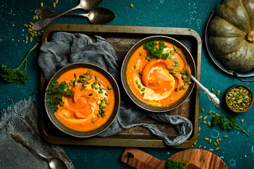 Two bowls of pumpkin porridge or cream soup with pumpkin seeds and cream. Autumn food concept. Top view.