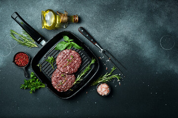 round burger patty with spices and herbs on a pan. Cooking a burger. On a dark stone background....