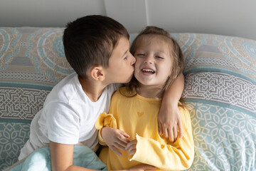 Brother kissing his little sister in bed at home