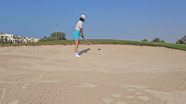 Girl golfer preparing for chipping the ball out of the sand trap concept