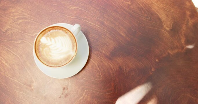 A cup of coffee with latte art sits on a wooden table in a cafe with copy space