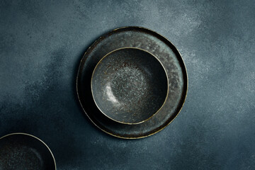 A set of dark ceramic bowls and plates. Close up on gray concrete background. Free space for text.