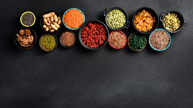 Superfoods and cereals selection in bowls: chia seeds, peas, green spirulina, goji berries and nuts, raisins, buckwheat, flax and quinoa. Free space for text.
