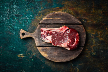raw cowboy steak with seasonings on a wooden board, prime rib eye on bone, top view. Top view.