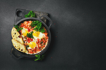 Tasty Breakfast Shakshuka in an Iron Pan. Fried eggs with tomatoes. On a black stone background.
