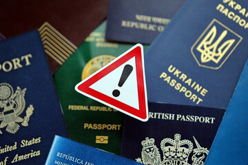 Many various passports of citizens of different countries and regions of the world and alert sign close up