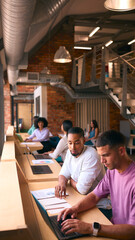 Two Businessmen With Laptop Meeting In Office Discussing Documents With Colleagues In Background