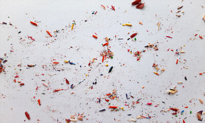 leftover shavings of colored pencil scattered on white paper, pencil flakes on white background, colored pencil shavings on white paper