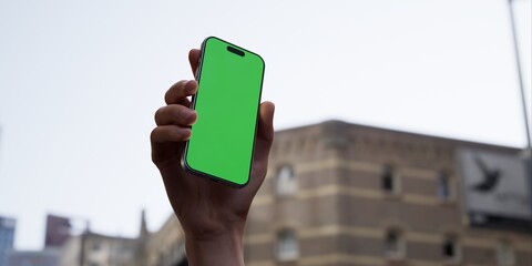 Hand holding a smartphone with a green screen on an urban city street background - 757291192
