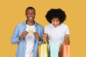 Excited African American couple with colorful shopping bags and a credit card - obrazy, fototapety, plakaty