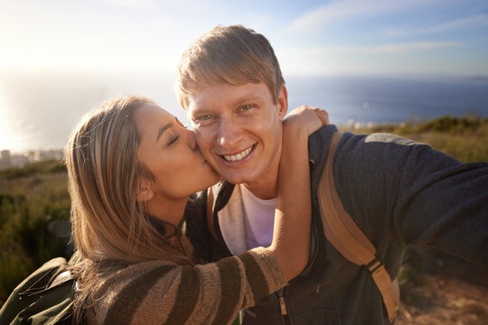 Hiking, kiss and fitness couple with selfie in nature for bonding, fun or romantic memory at sunset. Happy, love and people embrace for profile picture, photography or social media travel blog photo