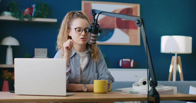 Blogger, content creator, radio host leading morning program. Female wearing glasses and talking in microphone. Woman radio presenter leading morning show. Radio host using table microphone.