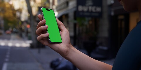 Hand holding a smartphone with a green screen on an urban city street background