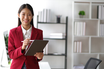 Portrait of attractive Asian businesswoman standing holding tablet in office.