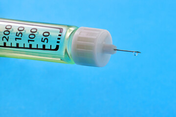 Drop of insulin on the needle tip of a syringe pen on a blue background