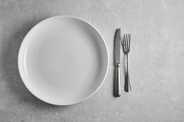 Empty white ceramic plate and fork and knife on gray stone table. Top view with a copy of the space