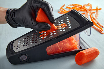 Cook in black latex gloves shreds carrots on a metal grater