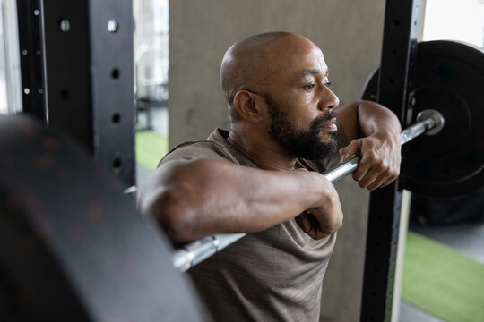 Mature African American male thinking about weight training goals with a barbell in a fitness gym