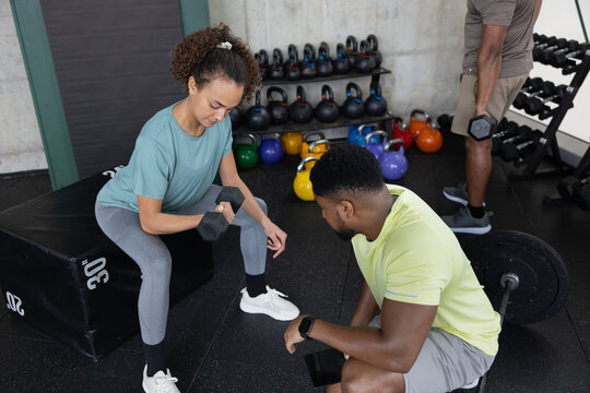 Gym instructor with female client using dumbbells for weight training 