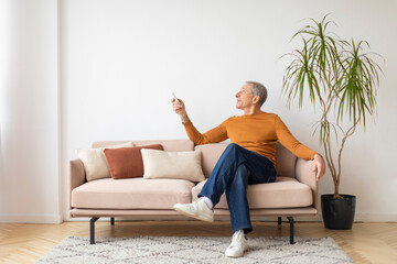 Senior man sitting on couch at home, turn on AC