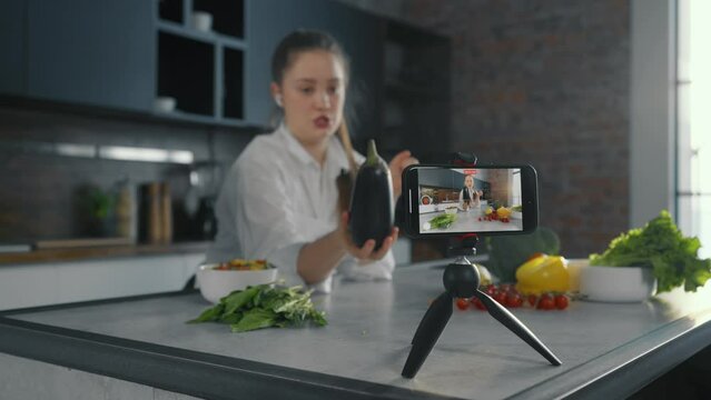 Young woman video lesson about cooking. Positive girl talks recording video lesson, filming cooks tutorial in loft kitchen studio. Concept for online chef cooking courses, recording of training.