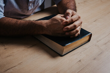 Man is praying with his hands together over the bible