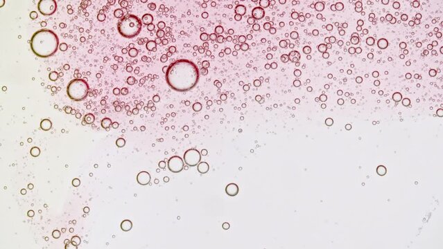 Transparent pink cosmetic gel fluid with bubbles oil on water white colored background. Macro Shot. High quality 4k footage