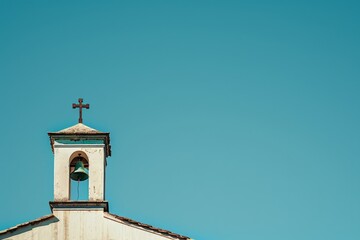 A photo of the top part of a church bell tower with a cross on it, against a clear blue sky background, in a minimalist, close-up shot Generative AI