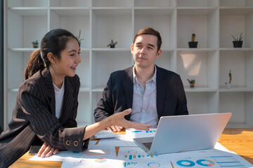 Two business people using a laptop ipad togerher in an office, a man and a women analyzing documents stat at office