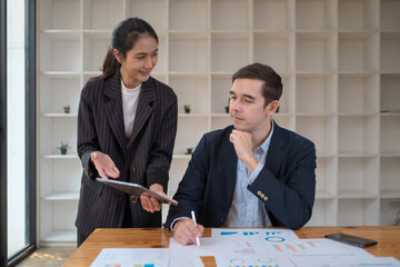Two business people using a laptop ipad togerher in an office, a man and a women analyzing documents stat at office