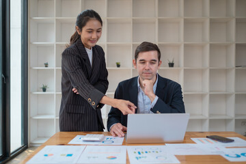 Two business people using a laptop ipad togerher in an office, a man and a women analyzing documents stat at office