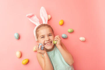Portrait of cute smiling girl with Bunny ears and yellow Easter eggs, isolated on pink background. Happy Easter