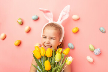 Portrait of cute smiling girl with Bunny ears and Easter eggs, holds spring bouquet of tulips, isolated on pink background. Happy Easter