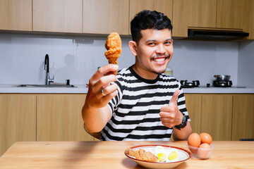 Funny asian man eating fried chicken and eggs at the kitchen © IgnatiusHarly