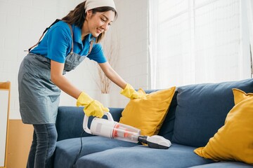 Using modern technology an Asian housekeeper diligently vacuum machine cleaners a sofa in a living...