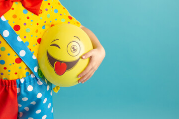 A bright yellow ball with a cheerful face in the hands of a clown child. Birthday and 1 April Fool's day concept