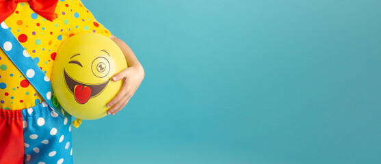 A bright yellow ball with a cheerful face in the hands of a clown child. Birthday and 1 April Fool's day concept