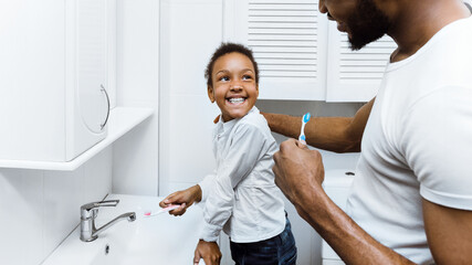 African-american girl brushing teeth with dad together