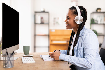 Cheerful black female student studying with headphones at computer