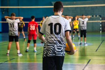 Team volleyball game at active match, rear view of guy in white black sportswear uniform with 10 number. Volleyball court in sport school gym. Sports games, team success concept. Copy ad text space
