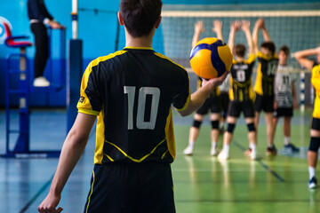 Rear view of guy in black yellow sportswear uniform with 10 number at active match. Team volleyball game, volleyball court in sport school gym. Sports games, team success concept. Copy ad text space