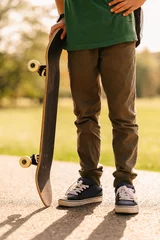 Foto op Canvas Faceless vertical outdoors shot of a teen boy holding his skateboard on a sunny day. © Vulp