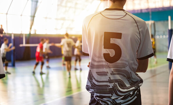 Team volleyball game at active match, guy in white black sportswear uniform with 5 number, rear view. Volleyball court in sport school gym. Sports games, team success concept. Copy ad text space