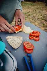 Close Up - Mädchen belegt beim Camping-Frühstück ein Brötchen mit Tomate und Käse