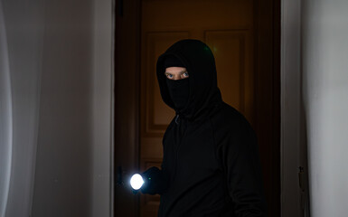 Masked robber with flashlight torch checking apartment. - 757349393