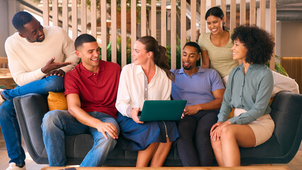 Multi-Cultural Business Team Sitting On Couch In Modern Open Plan Office Working On Laptop Together