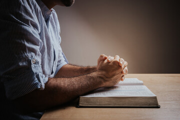 Man is praying with his hands together over the open bible, side view