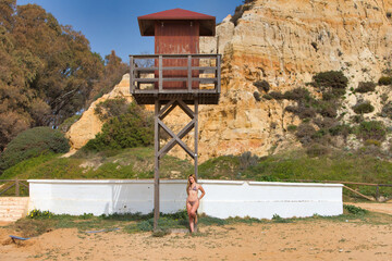 Pretty young blonde woman leaning on the wooden poster of the lifeguard tower on the beach. The woman is wearing a leopard bikini and enjoying her summer holiday.